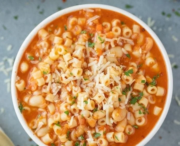Bowl of rich Pasta Fagioli soup with beans and pasta, garnished with herbs.