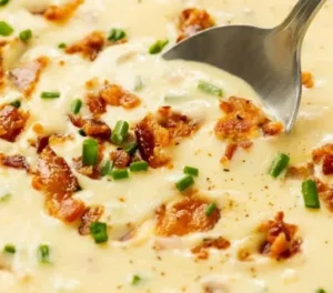 A bowl of creamy baked potato soup garnished with chives and cheese.