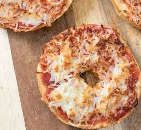 Air Fryer Bagel Pizzas Recipe: Quick Dinner 2 Air fryer bagel pizzas topped with cheese and pepperoni on a wooden cutting board